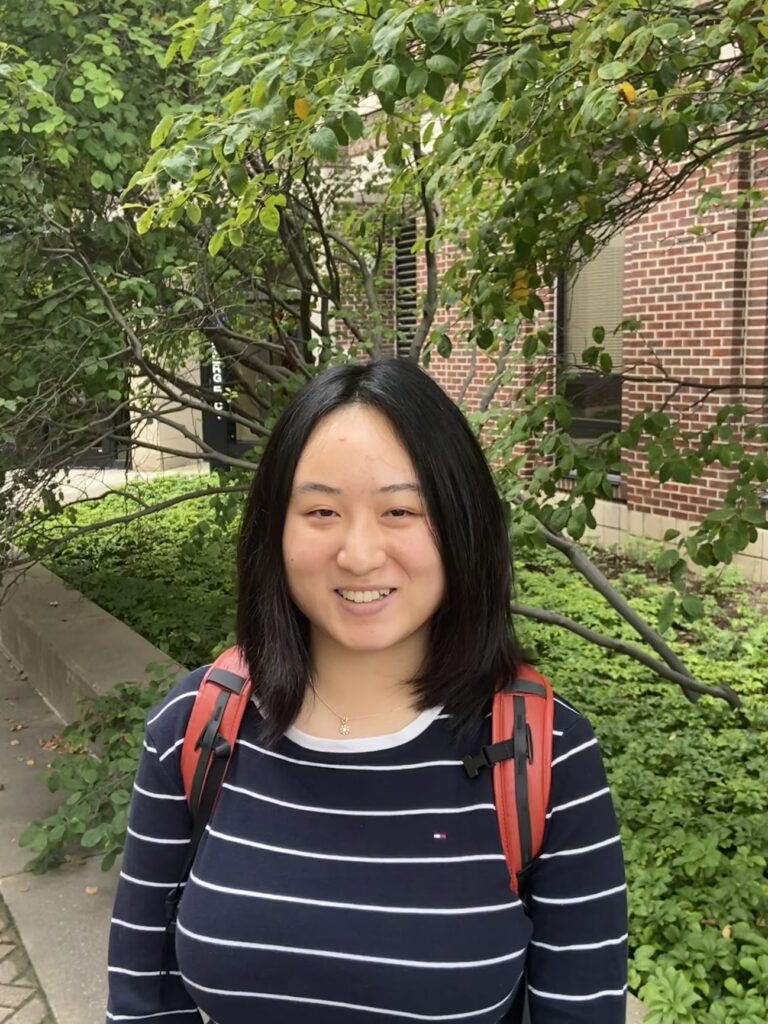 Tian smiles before a tall tree, ready to provide psychotherapy and mental health services.